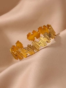 Détail du bracelet ouvert doré à texture florale posé sur un tissu en satin élégant