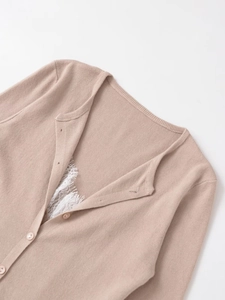 Close-up of beige knitted cardigan featuring white eyelash lace trim and V-neck buttons