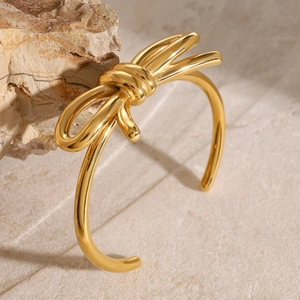 Minimalist gold bow-shaped stainless steel open bangle displayed on a natural stone base