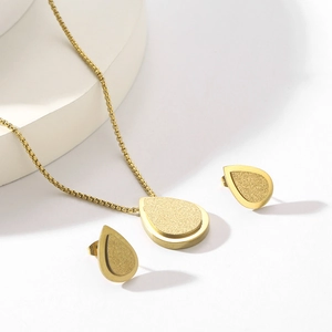 Detail view of gold teardrop jewelry set with necklace and earrings on white pedestal