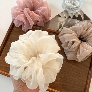 Close-up of pink, beige, and light brown tulle scrunchies on a wooden tray with a hand