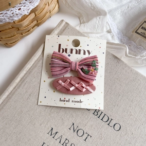 Detailed flat lay of handmade pink fabric hair clips with floral embroidery and bow
