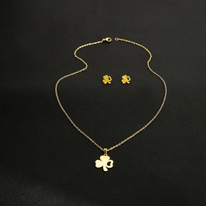 Detailed view of golden clover necklace and earrings set on black leather background