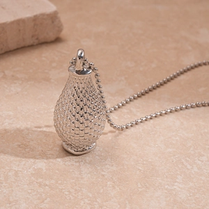 Détail du pendentif bouteille argenté avec texture tissée sur fond de marbre