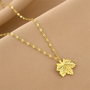 Golden maple leaf pendant necklace with textured veins on elegant beige fabric background