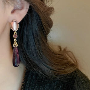 Detail of gothic vintage teardrop earrings with pink cat-eye stone and purple rhinestones