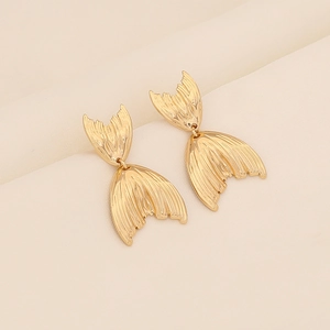 Golden fishtail stainless steel earrings with brushed metal texture on beige fabric