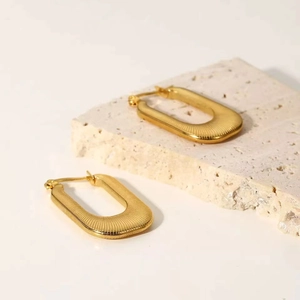 Detailed view of textured gold U-shaped stainless steel earrings on a stone surface