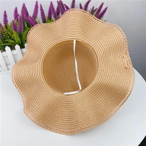 Detail of straw sun hat with wavy brim and white windproof strap on white table