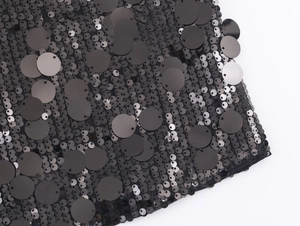 Close-up of black sequin fabric detail showing layered texture and glossy reflection