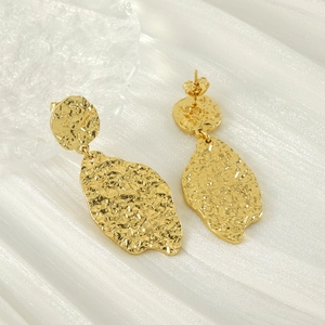 Close-up of golden irregular leaf earrings with hammered texture on silk fabric