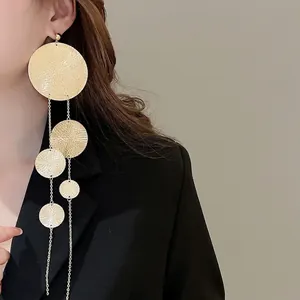 Exaggerated gold hammered metal disc tassel earrings worn by a model in a black suit