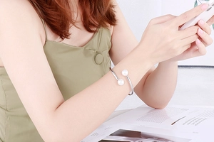 Detail view of a silver open pearl bracelet worn on a wrist in a lifestyle setting