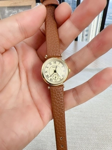 Detail of a vintage-style women's quartz watch with gold case and brown leather strap