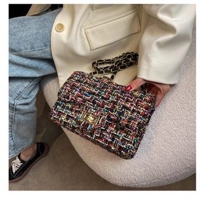 Detail of tweed crossbody bag with golden chain strap and lock on a beige suit