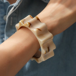 Dettaglio di un bracciale ampio ondulato in acrilico con venature marmoree su denim blu