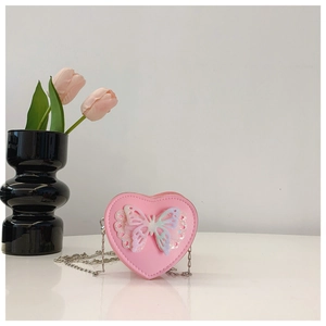 Pink heart-shaped girl's crossbody bag with chain and butterfly detail in indoor setting