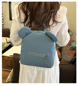 Rear view of a light blue denim backpack with cute bear ears worn in a cozy home setting