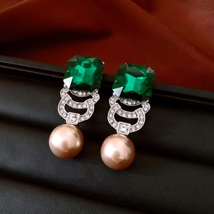 Detail of vintage square green gem earrings with rhinestone accents and dangling beige pearl