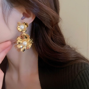 Détail de grandes boucles d'oreilles fleurs dorées avec perles portées par un mannequin