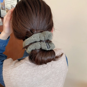Close-up of a green knitted scrunchie with a Fashion tag on a brunette bun hairstyle