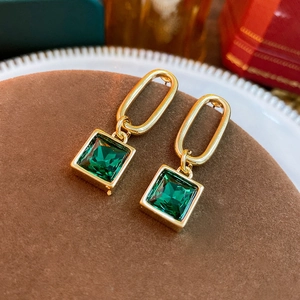 Close-up of vintage gold earrings with square green stones on a brown velvet display