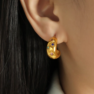 Gold-plated C-shaped earrings with colorful gemstones worn by a fashion model