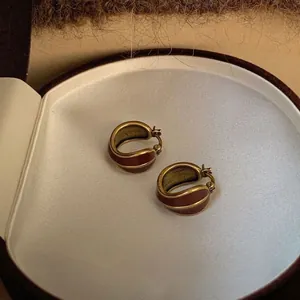 Detail shot of vintage C-shaped gold earrings with dark brown enamel inside a jewelry box