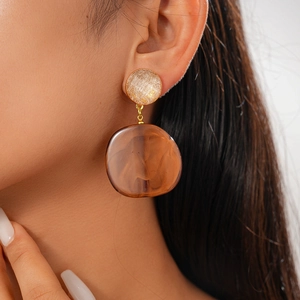 Close-up of amber resin drop earrings with circular studs on model's ear