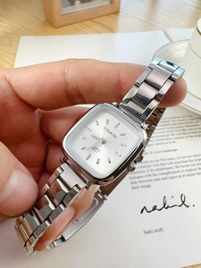 Close-up of a silver square quartz watch with a white dial and metal strap worn on a wrist