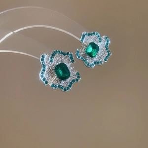 Macro detail of silver flower stud earrings with emerald cut green stone and pave zircons