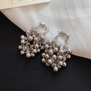 Détail de boucles d'oreilles grappes de perles argentées sur fond noir et soie blanche