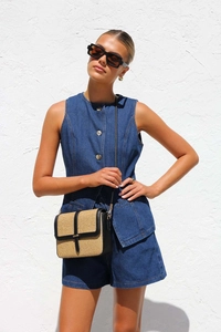 Détail d'un costume sans manches en denim bleu foncé et d'un sac en paille tissée sur mur