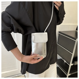Close-up of a silver metallic crossbody phone bag with flap and thin strap on a model