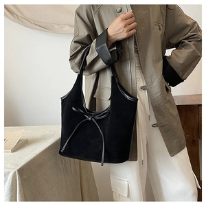 Detail of a large black suede tote bag with decorative bow on a female model