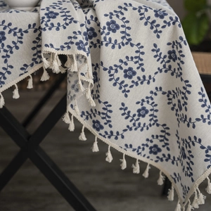 Detail of beige linen tablecloth with blue floral vine pattern and tassel edge finish