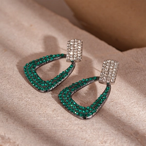 Detailed view of geometric teardrop earrings with green crystals on a stone background