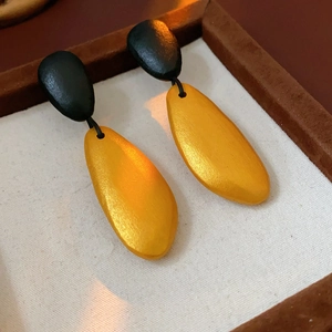 Close-up of irregular black and gold water drop earrings on fabric inside a wooden box