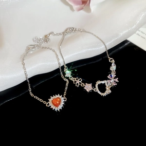 Detail of silver charm bracelet featuring a zircon heart and cat pendant on a reflective surface