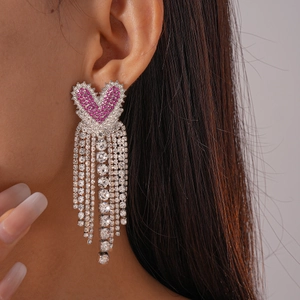 Détail de boucles d'oreilles cœur rose avec pampilles en strass argentés sur un mannequin