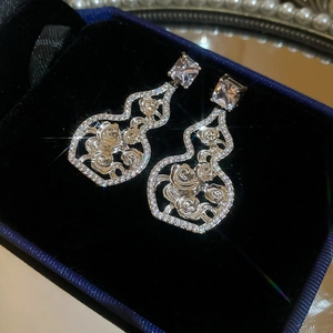 Macro shot of silver hollow gourd drop earrings with zircon roses in a blue jewelry box