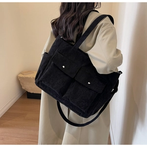 Detail of black corduroy tote bag showing front flap pockets and versatile shoulder straps