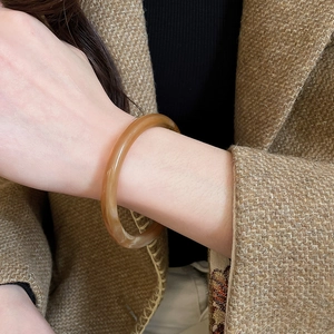 Gros plan détaillé d'un bracelet jonc lisse en résine ambrée couleur miel au poignet