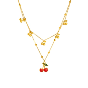 Collana a doppio strato dorata con ciondoli a forma di ciliegia rossa e foglie su sfondo bianco