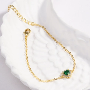 Gros plan du bracelet doré avec pendentif cœur vert émeraude et fermoir mousqueton