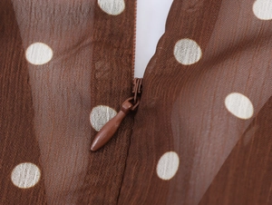 Détail de la fermeture éclair invisible sur une robe en mousseline marron à pois blancs