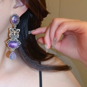 Detail of vintage cat earrings with purple gemstones and silver relief design
