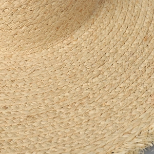 Détail macro du chapeau de paille montrant le tissage serré et le bord effiloché chic