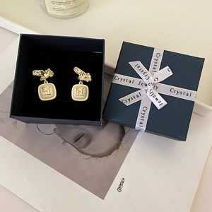 Detail of gold enamel H-letter earrings inside a navy jewelry box with white ribbon