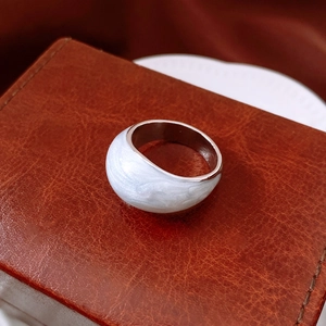 Dettaglio macro di un anello in smalto bianco e argento su una texture in pelle marrone